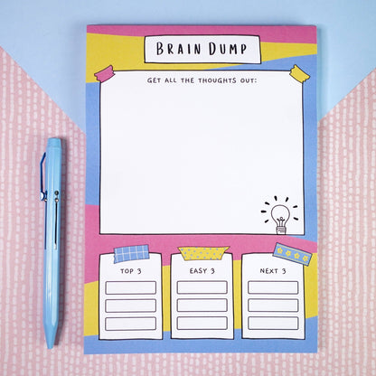 ADHD A2 brain dump notepad with 'Brain Dump' design on a pink and blue textured background, next to a light blue pen