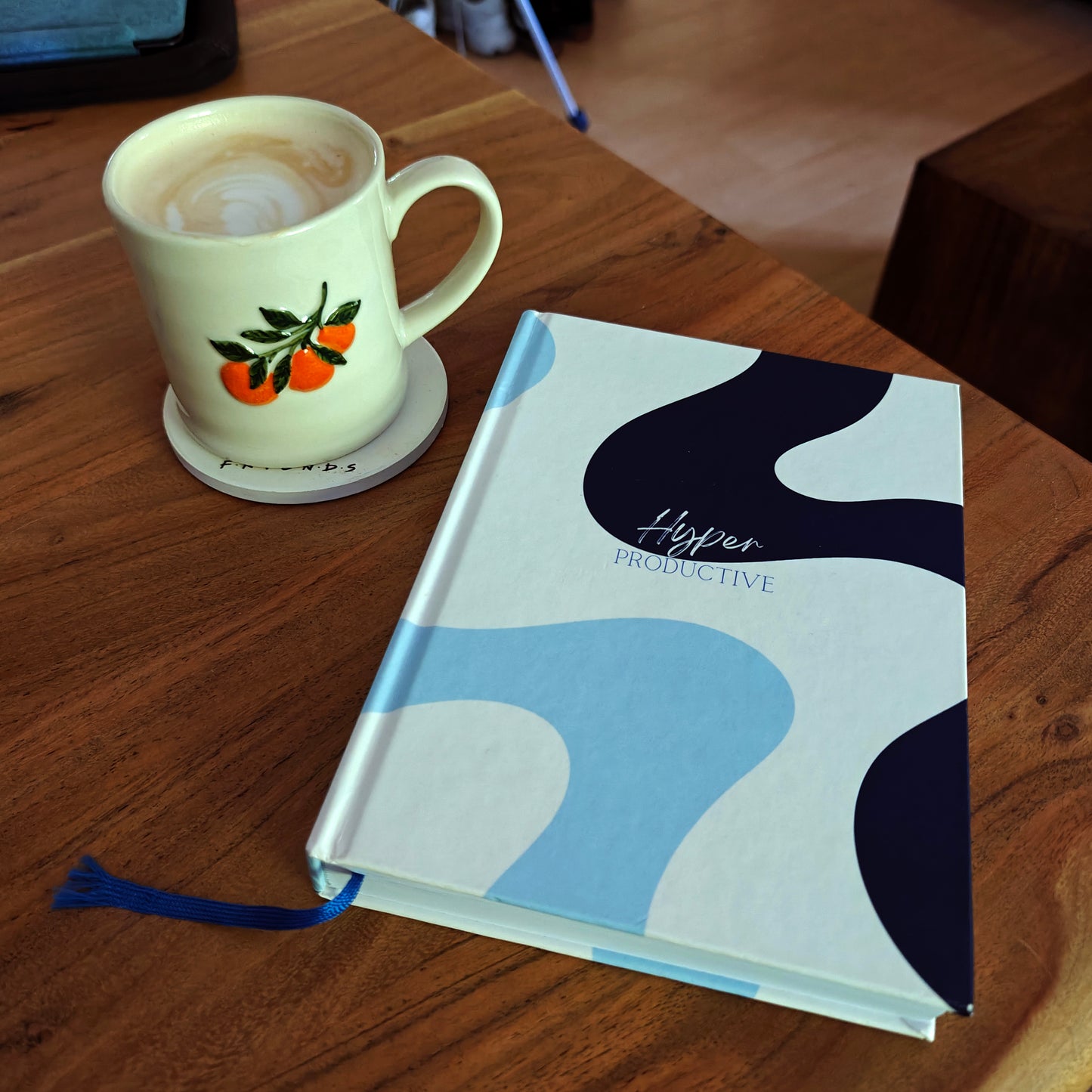 An ADHD daily planner with abstract design on a wooden table next to a coffee mug with orange design.