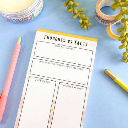 ADHD thoughts vs facts notepad on a blue surface with stationery items and washi tape