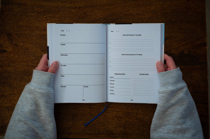 Person holding an open ADHD daily planner open on the weekly calendar and goal setting spread, on a wooden desk