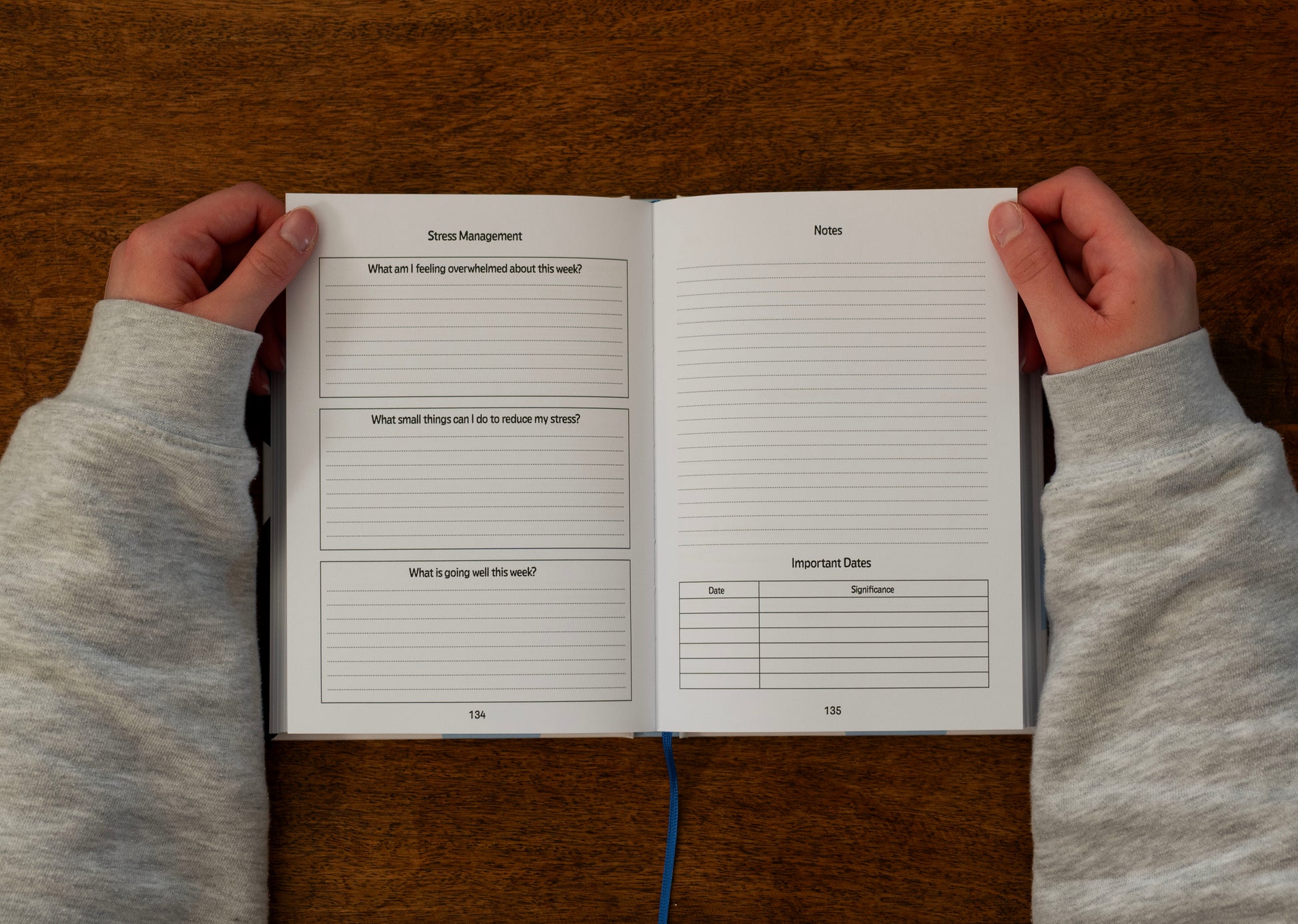 Person holding an ADHD daily planner open on the stress management, notes and important date tracking spread, on a wooden desk