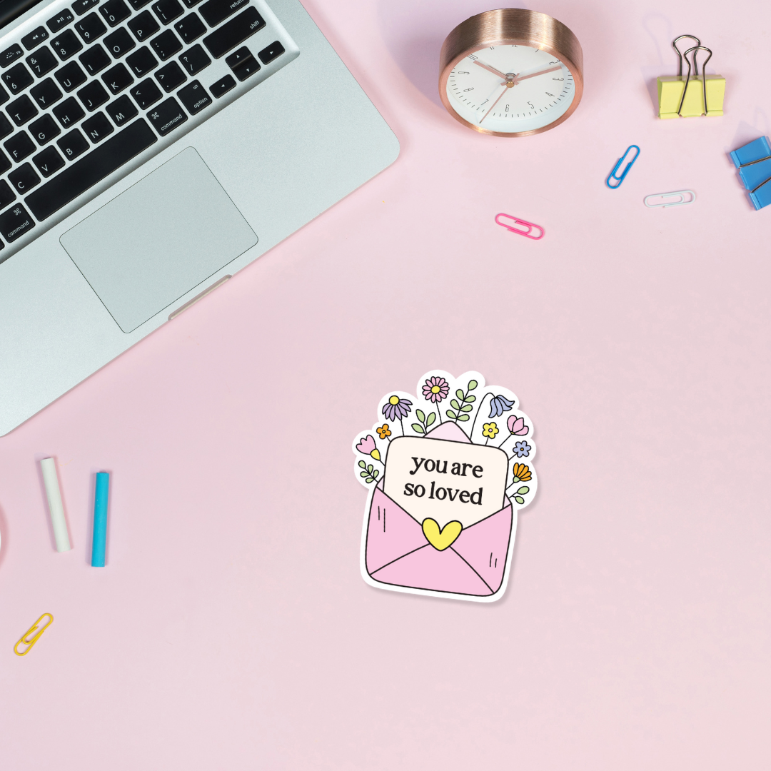 ADHD vinyl sticker with 'you are so loved' text on a pink surface with laptop and stationery items